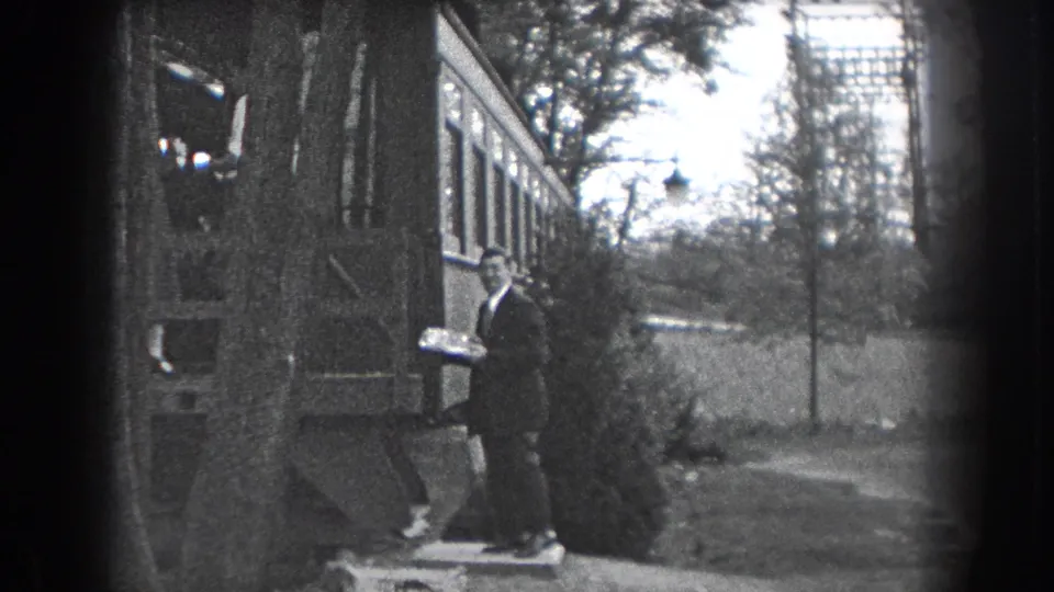 A suited man holds a cake or tray outside a Reading, Pennsylvania house in 1938 home-movie footage.