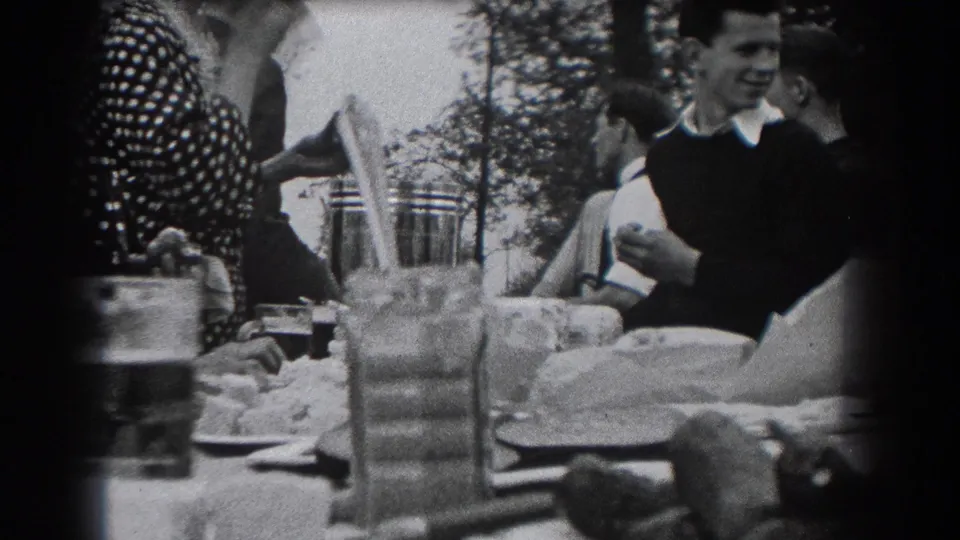 Adults at a 1938 outdoor meal in Reading, Pennsylvania, with a smiling man and nearby diners framed beside tableware and trees.
