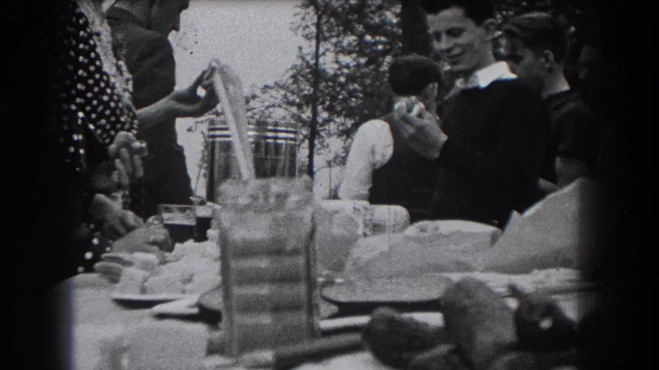 Reading, Pennsylvania picnic scene from 1938 showing adults gathered around a table as one man smiles near stacked dishes and cups.