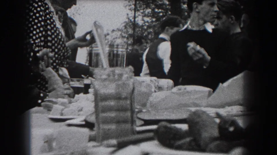 Late-1930s home-movie frame from Reading, Pennsylvania showing adults at an outdoor meal, with dishes and drinkware spread across the table.