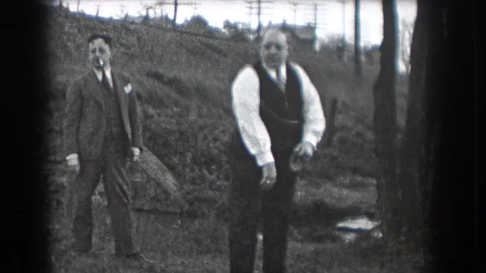 In this 1938 Reading, Pennsylvania frame, two men stand outdoors on a hillside area near trees and utility poles.