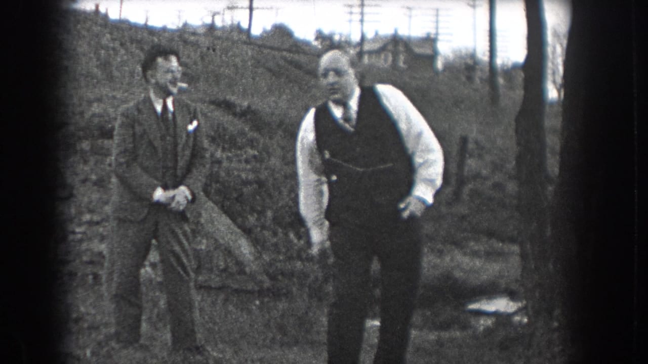 Two men in dress clothes stand outdoors near a sloped embankment.