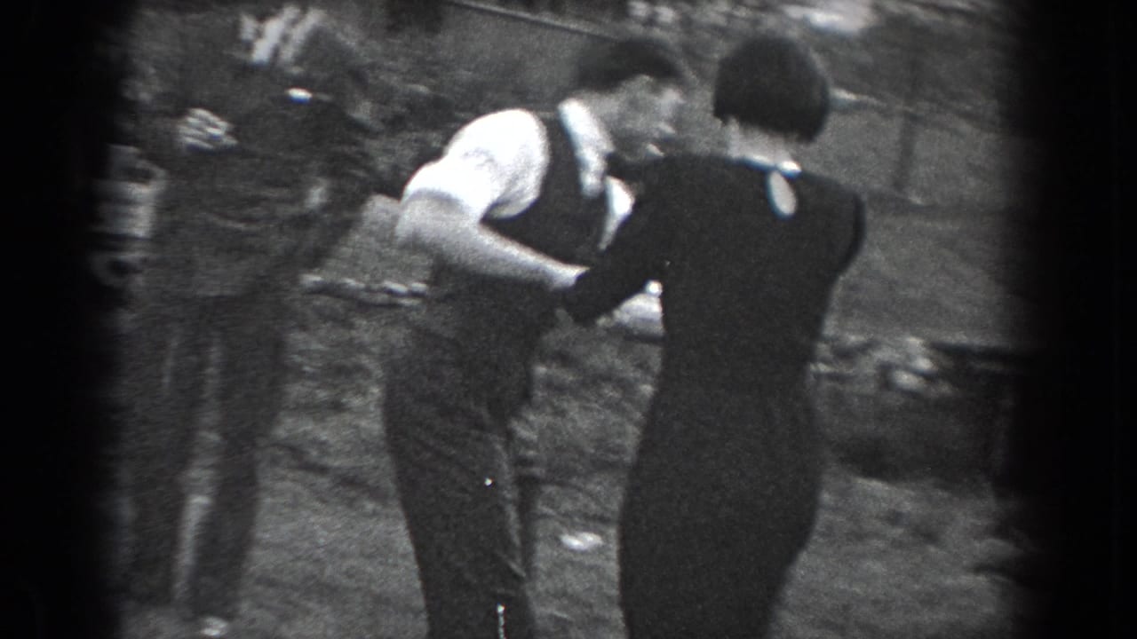 A couple dances closely on a lawn while other adults stand nearby.