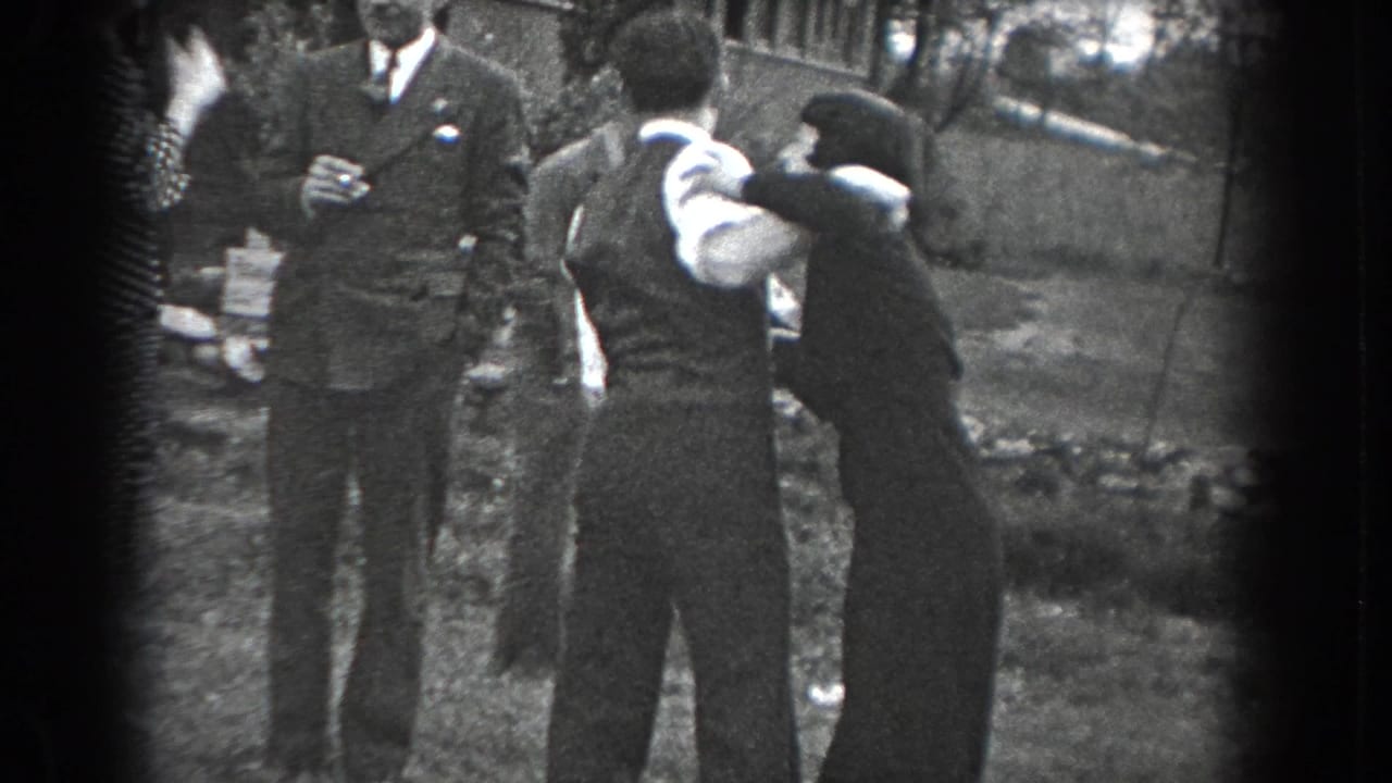 The couple continues dancing in close embrace in the Reading, Pennsylvania lawn scene, with suited and formally dressed guests nearby.