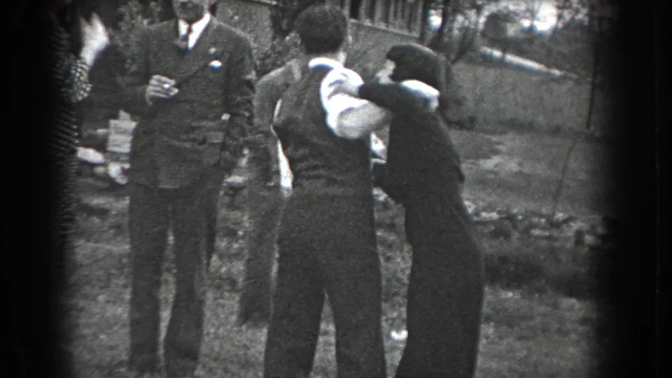 The couple continues dancing in close embrace in the Reading, Pennsylvania lawn scene, with suited and formally dressed guests nearby.
