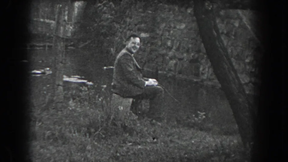 A man sits outdoors near a body of water in Reading, Pennsylvania, with trees, rocks, and a stone wall around him.