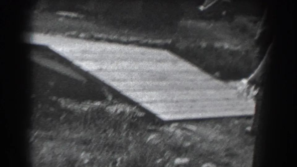 1938 Reading, Pennsylvania home-movie frame showing a shadowed wooded area with a wooden ramp or walkway and partial people near the frame edge.