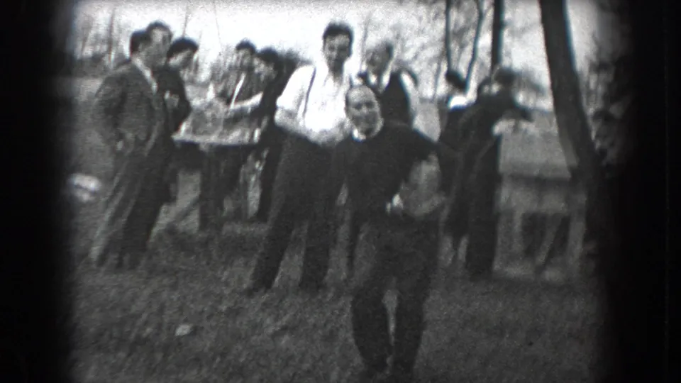 1938 Reading, Pennsylvania frame showing a person walking toward the camera with several adults gathered behind in a wooded recreation setting.