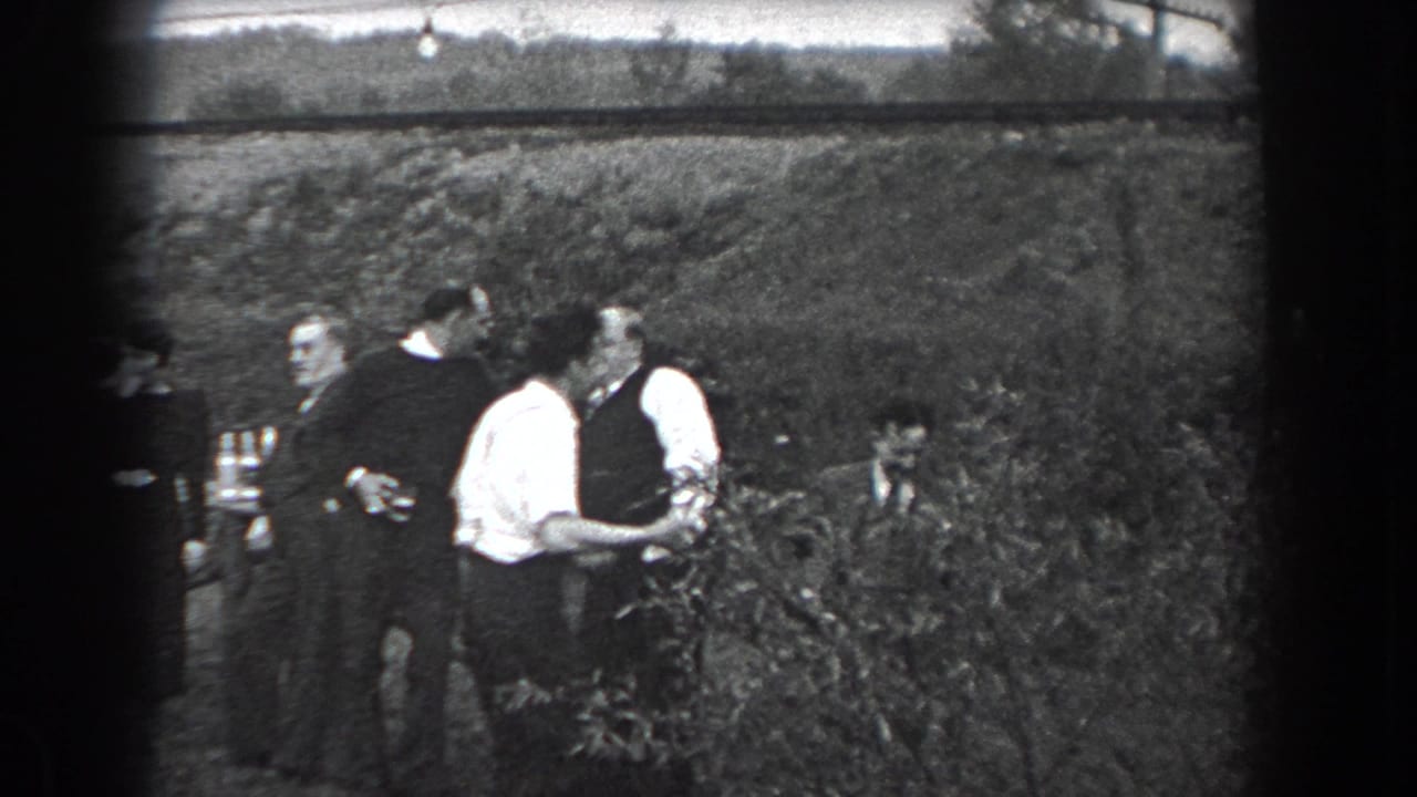 In 1938 Reading, Pennsylvania, adults in period clothing stand and talk near an outdoor table by a grassy hillside.