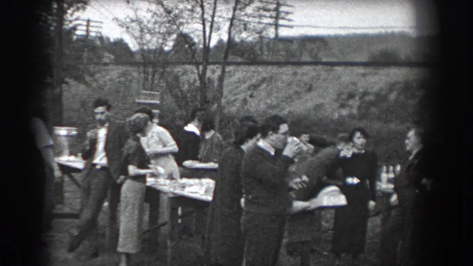 Adults in period dress eat, drink, and talk beside serving tables at the Reading, Pennsylvania gathering.