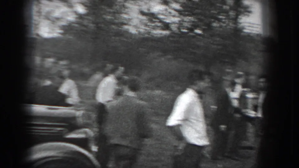 1938 Reading, Pennsylvania home-movie frame showing suited men gathered near a dark classic car in a park-like setting.