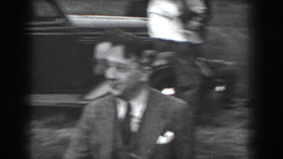 In 1938 Reading, Pennsylvania home-movie footage, a suited man smiles toward the camera near a partially visible parked automobile.