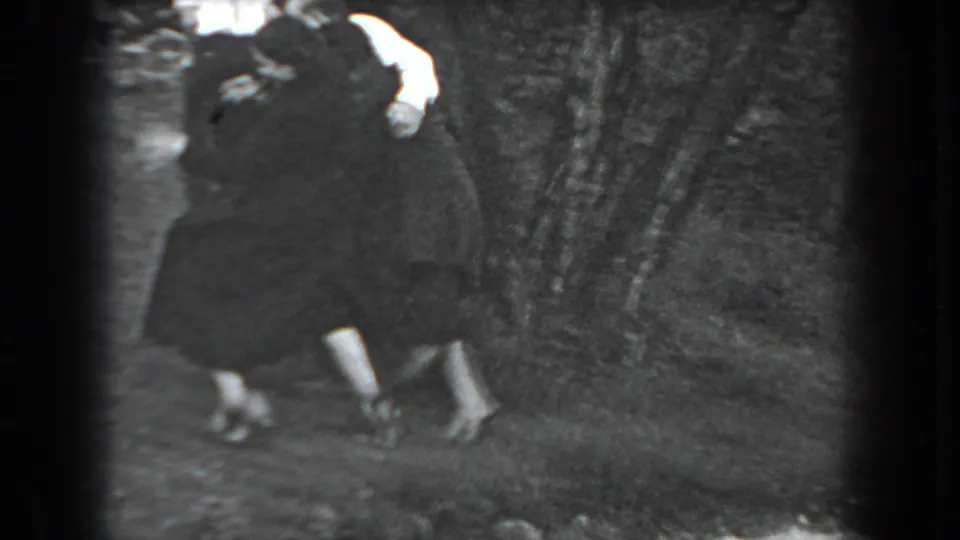 Two adults appear to embrace or stand closely together near shrubbery in the 1938 Reading, Pennsylvania home-movie scene.
