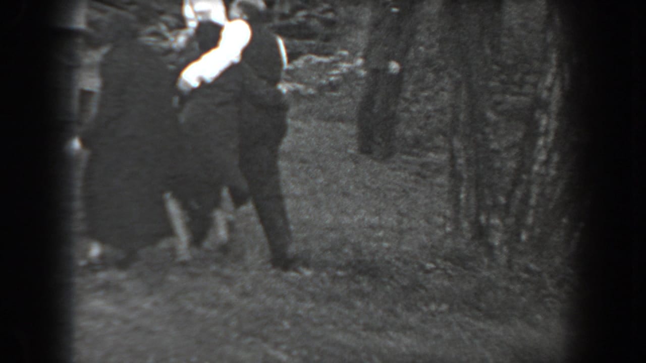 In Reading, Pennsylvania, 1938, adults in dark clothing gather outdoors while a woman in white gloves gestures toward the camera.
