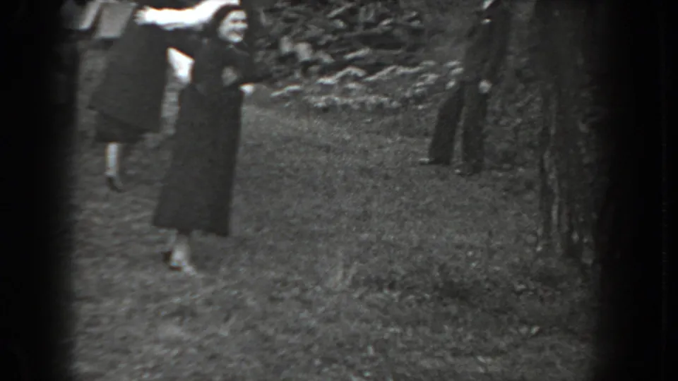 A woman in a long dark coat raises her arms toward the 8mm camera in a grassy Reading, Pennsylvania outdoor scene from 1938.