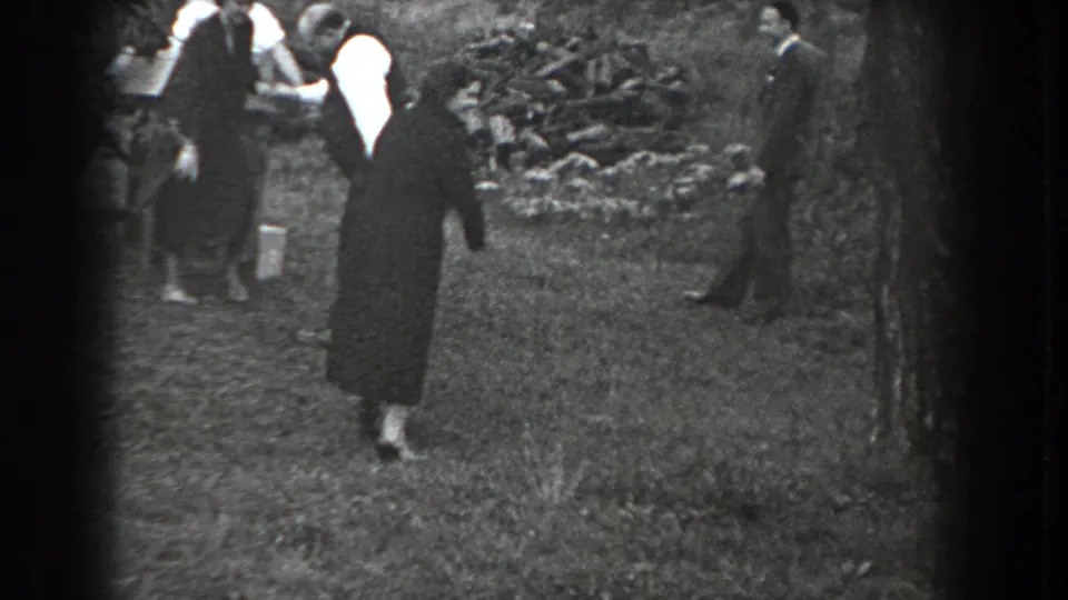 A dark-coated woman moves across the grass as several adults stand nearby in this 1938 Reading, Pennsylvania home-movie frame.