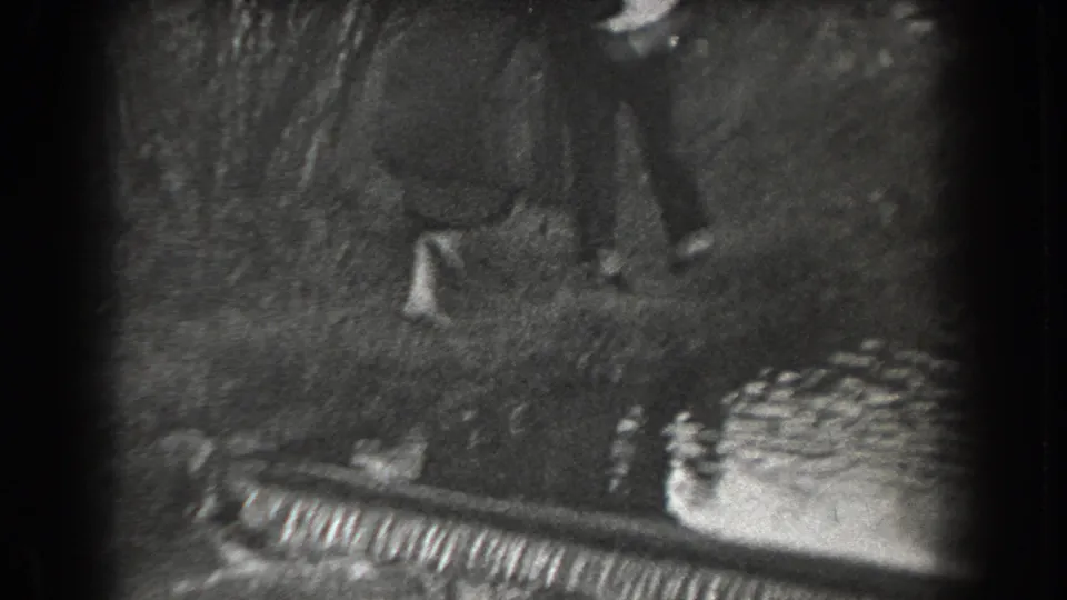 1938 Reading, Pennsylvania home-movie frame showing adults partly visible near grass, trees, and a small water edge.