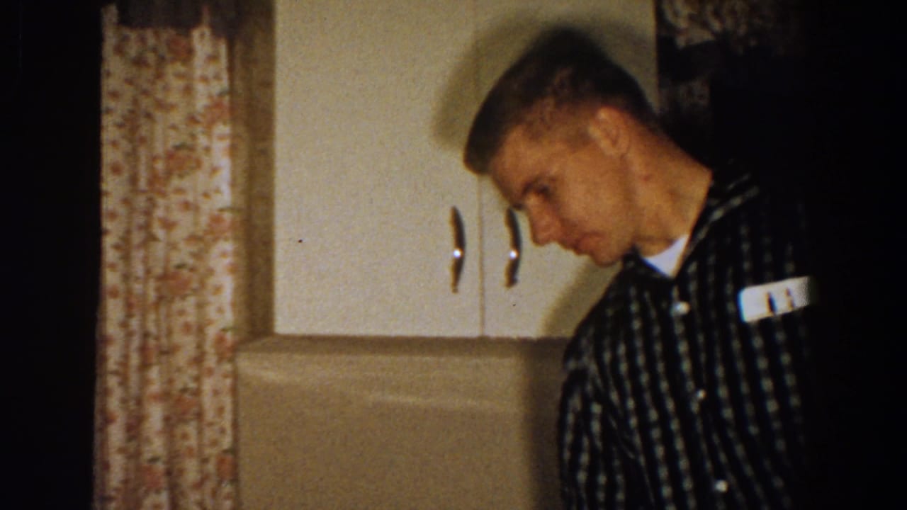 Man in checkered shirt leaning near kitchen cabinets.