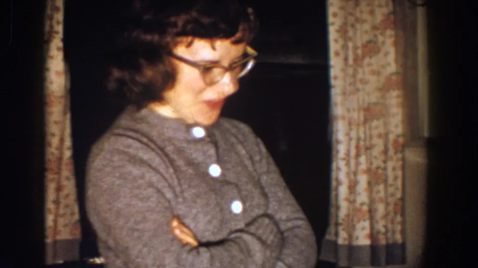A woman with dark hair and glasses stands with folded arms in the Aliquippa kitchen, wearing a gray buttoned sweater.