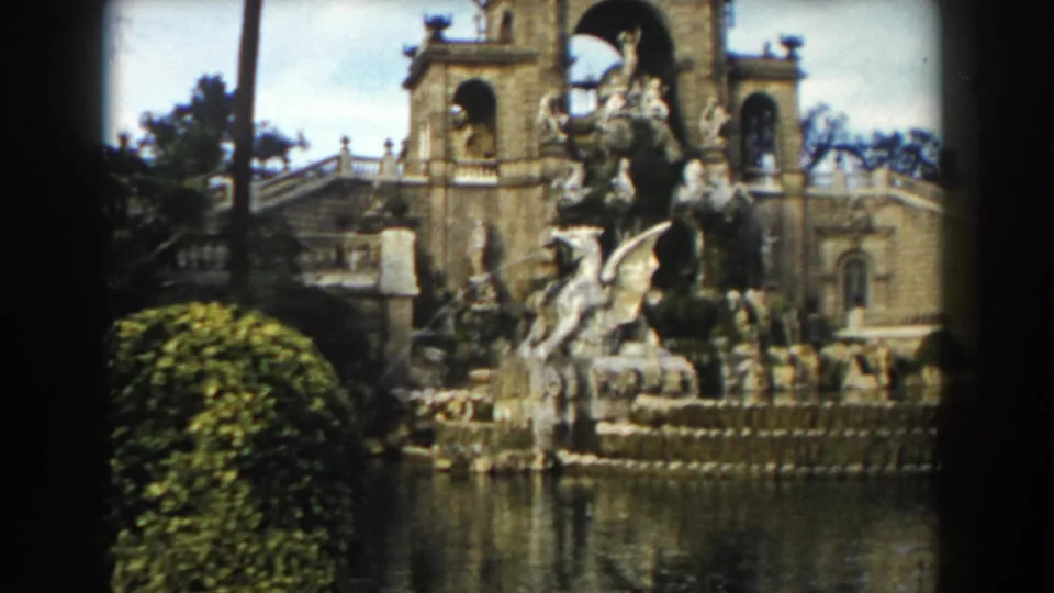 1959 Barcelona home-movie view of an ornate fountain complex, with sculpture, water, hedges, stairs, and classical stone architecture.