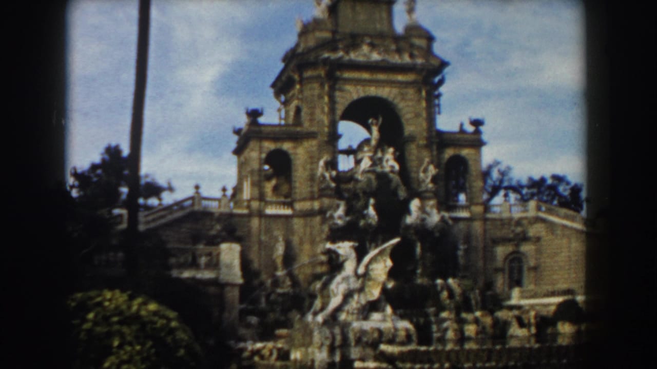Ornate stone monument with sculptures, palm trees, and blue sky in a dark-edged 8mm frame.