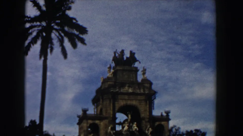 1959 Barcelona frame showing the ornate monument shifted right, with a palm tree silhouetted against the sky and visible 8mm frame edges.
