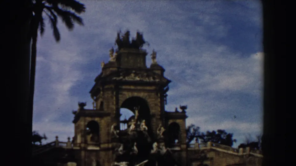 1959 Barcelona frame of the monument's upper section, with carved stonework, arches, sculpture, and a palm frond near the top edge.