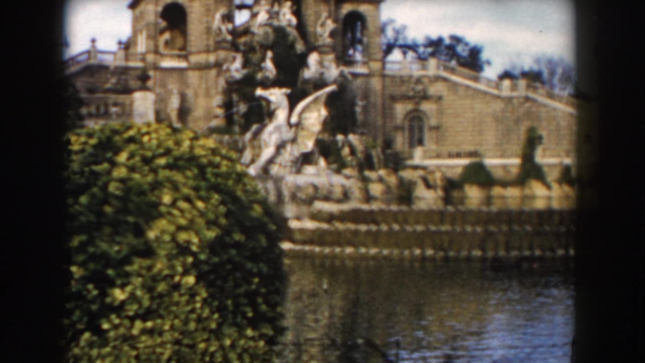 Closer view of sculptural fountain, hedge, water, and arched stone architecture.