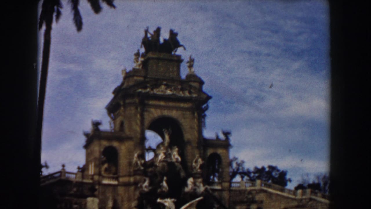 Stone arch monument with fountain sculpture beneath a blue sky.