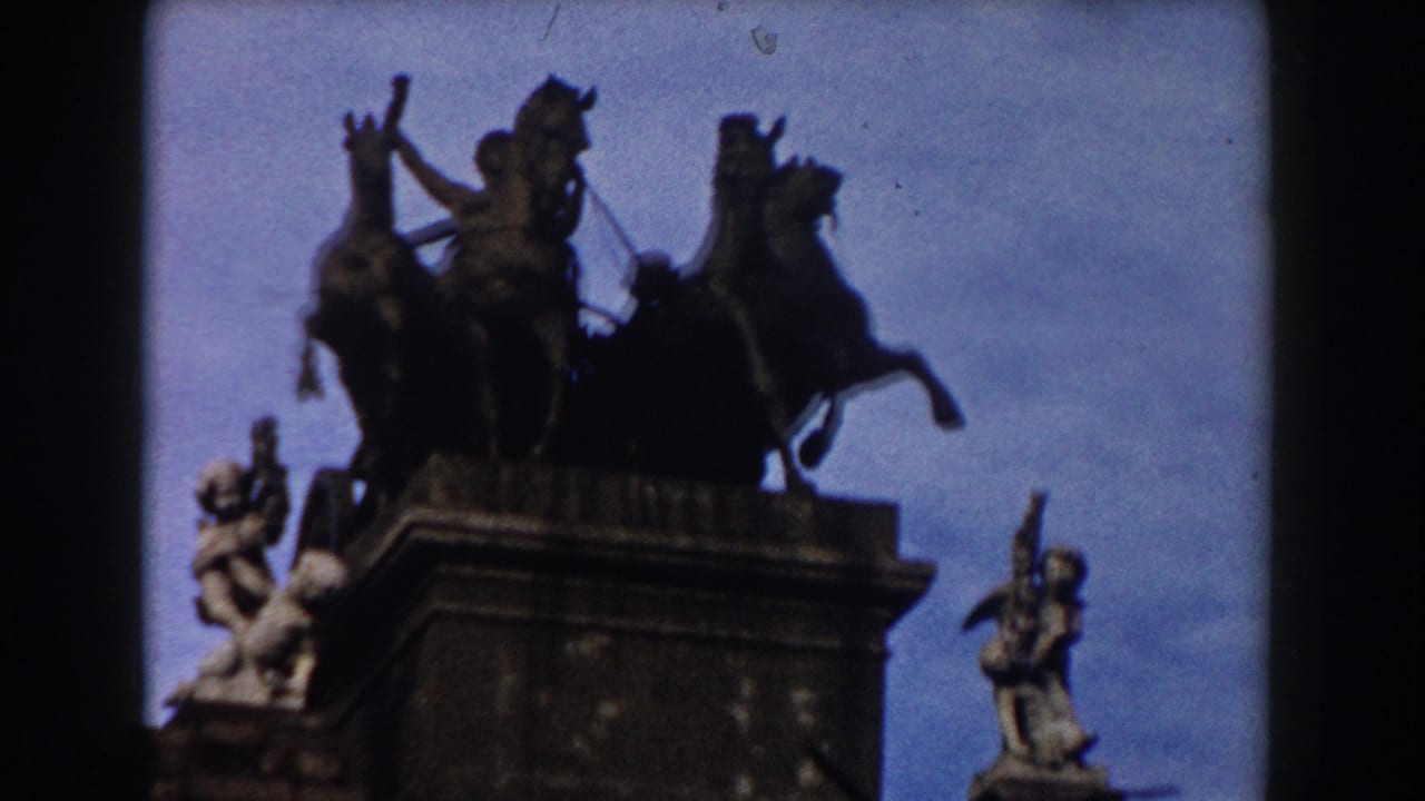 1959 Barcelona home-movie frame showing a silhouetted horse-and-chariot monument above a historic stone gateway.