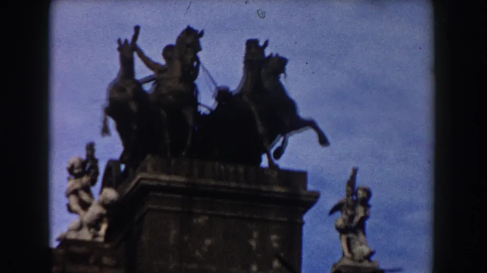 1959 Barcelona home-movie frame showing a silhouetted horse-and-chariot monument above a historic stone gateway.