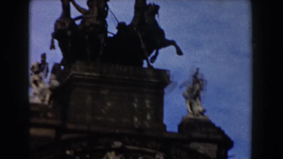 Closer 8mm view of the Barcelona gateway's upper monument, with horse figures and flanking sculptural details.