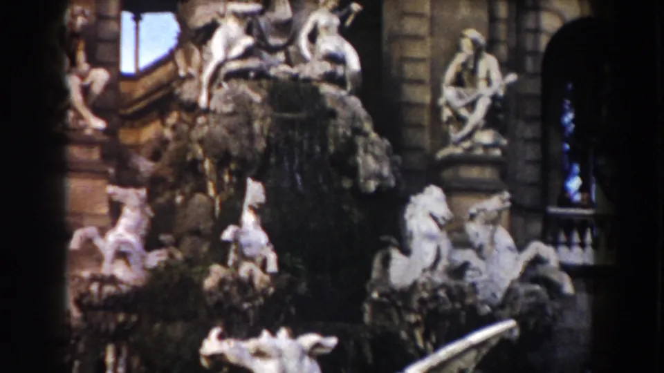 Barcelona home-movie frame showing ornate fountain sculpture, white classical figures, and architectural stonework.