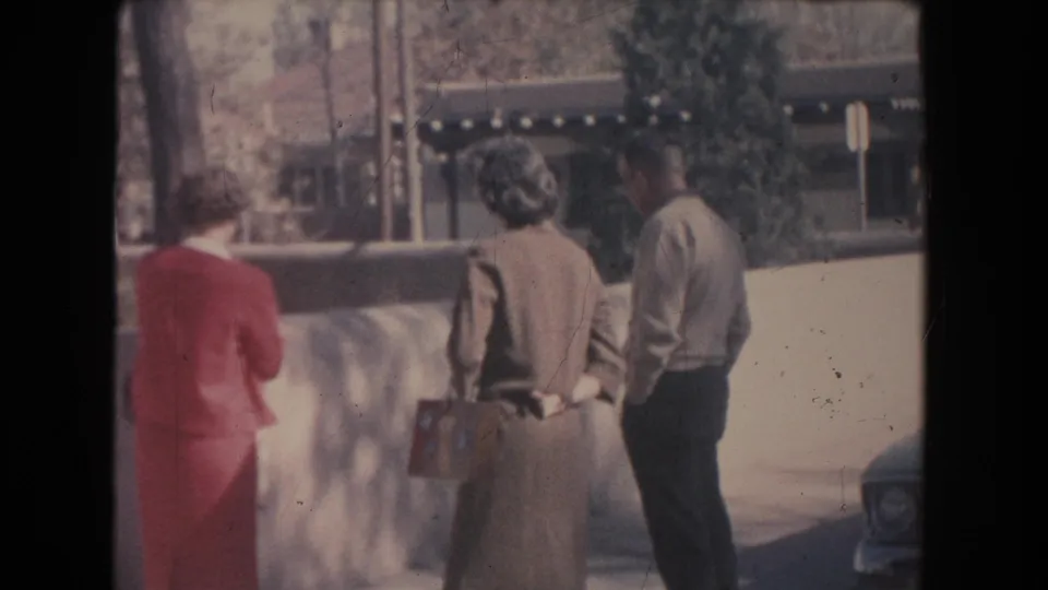 The final frame shows the group still facing the low wall, with trees, a signpost, building details, and a car edge visible.