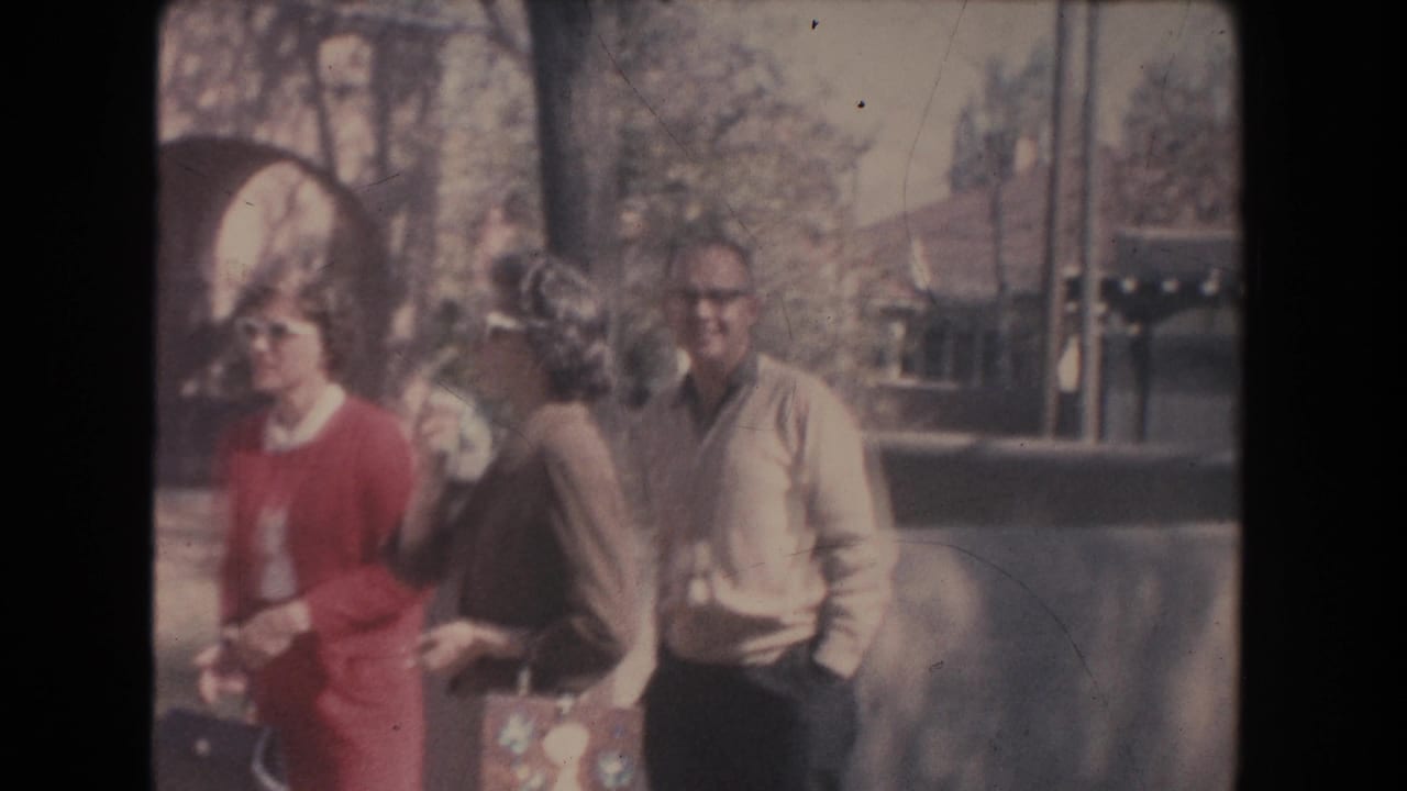 Three adults walking outside near arched doorways and shrubs.