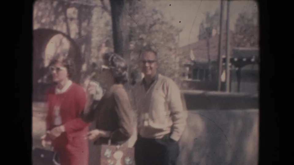 1951 New Mexico home-movie frame showing two women and a man walking outside near arched doorways and landscaping.