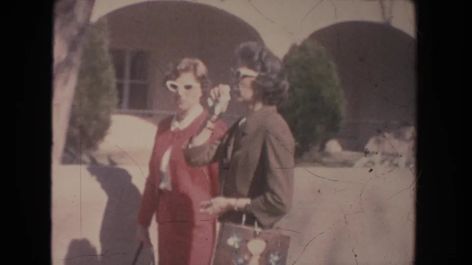 1951 New Mexico home-movie frame showing two women close to camera, with arched doorways and shrubs behind them.