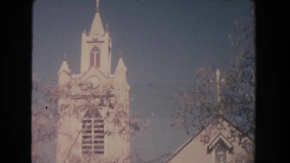 1951 New Mexico 8mm frame showing a white church steeple and facade partly screened by trees in bright daylight.