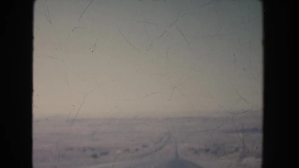1951 New Mexico 8mm frame looking out across a broad pale plain with faint road or track lines under a hazy sky.