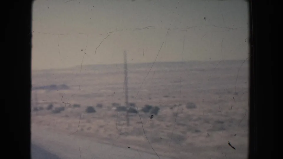 1951 8mm roadside view in New Mexico showing utility poles across an open desert plain with sparse brush and a hazy horizon.