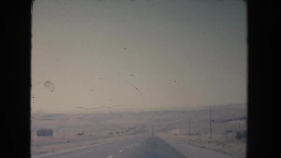 1951 New Mexico home-movie frame looking down a paved highway through sparse desert terrain, with utility poles and muted film color.