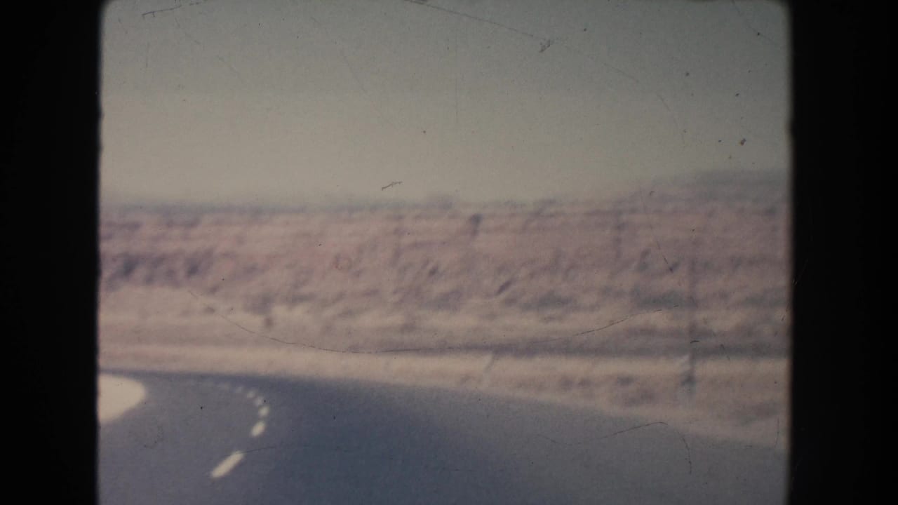 1951 New Mexico home-movie frame showing a winding paved road through arid valley terrain under a hazy sky.