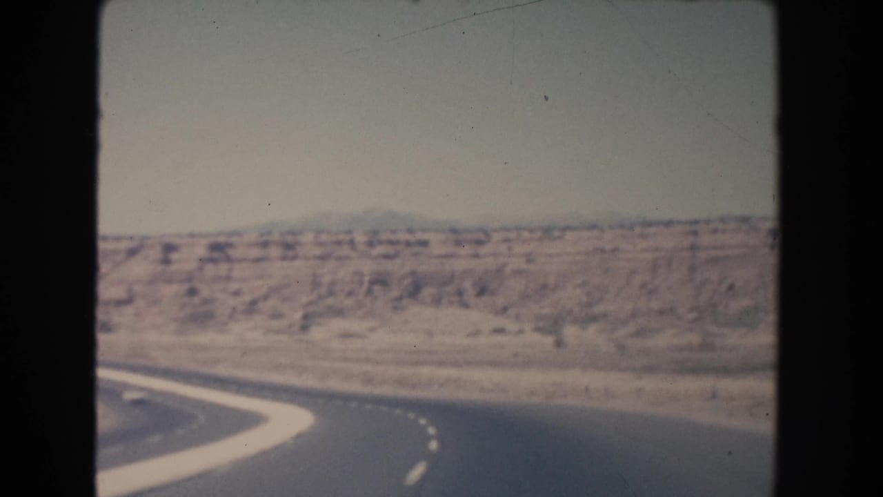 Paved road bending through open arid terrain with distant low hills.