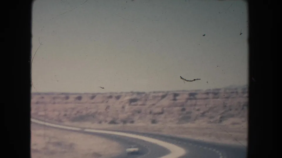 1951 New Mexico highway view from a moving car, with dry hills and a small vehicle near the curve.