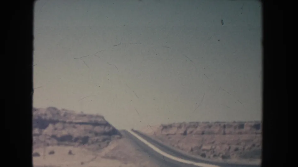 1951 New Mexico home-movie frame showing a paved road climbing through arid hills with soft faded color.
