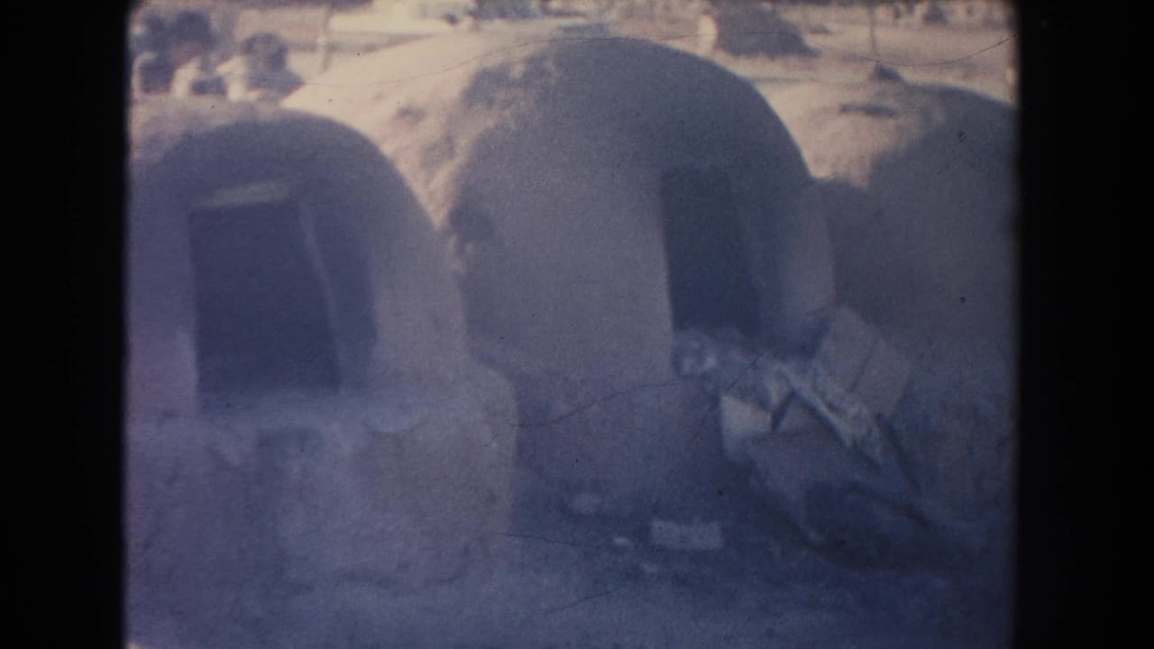 Closer view of adobe dwellings with dark entrances and indistinct roadside activity behind.