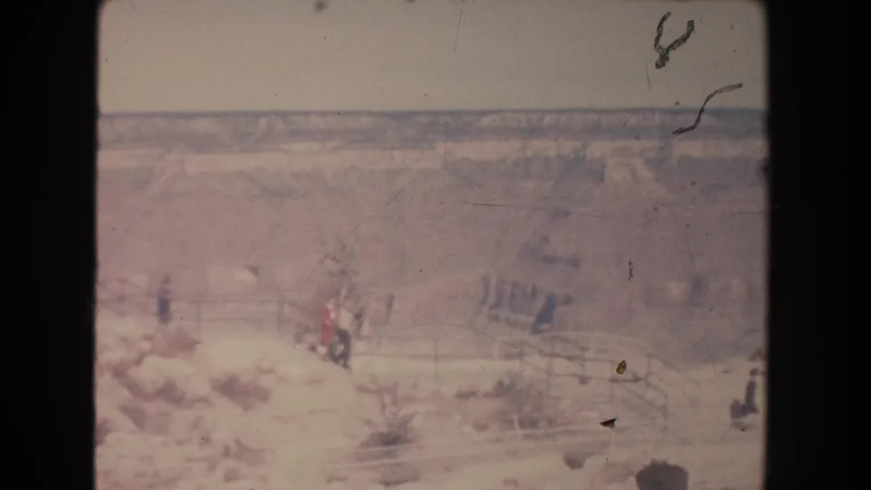 1951 New Mexico home-movie frame showing distant visitors on a bright canyon overlook path with railings and pale rock forms.