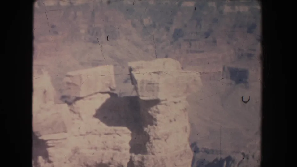 Washed 8mm view of beige canyon boulders and rough stone surfaces, likely part of the New Mexico overlook sequence.