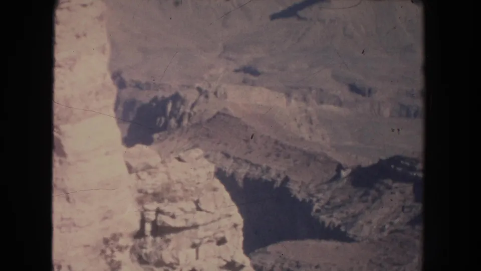 1951 8mm home-movie frame showing layered canyon rock, pale cliff faces, and dark shadowed terrain.