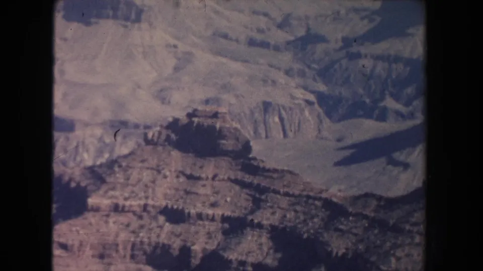 Wide 8mm view of a canyon landscape with terraced rock layers, pale slopes, and dark recessed areas.